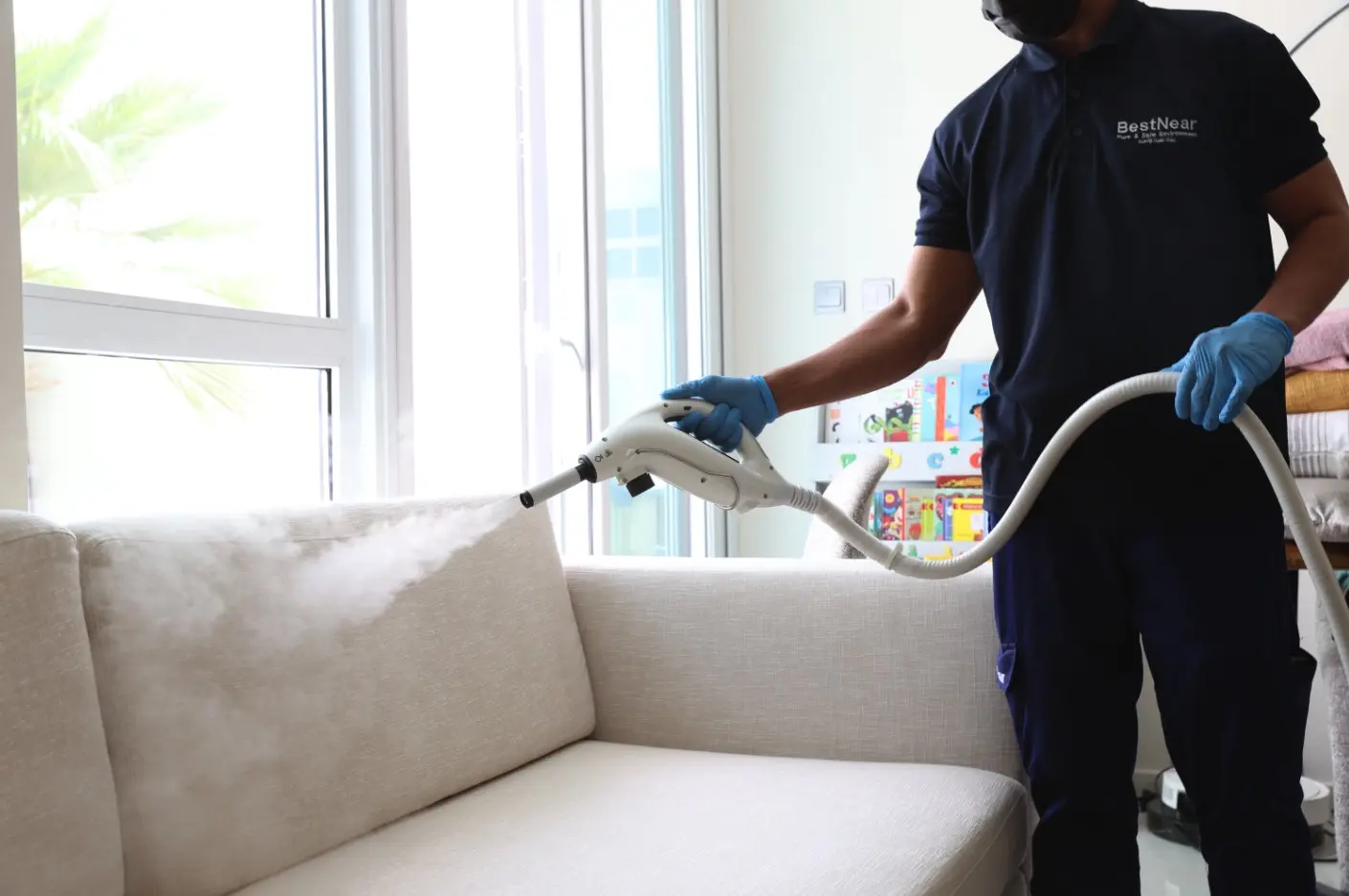 A BestNear technician steam-cleaning a light-coloured sofa in a Dubai home