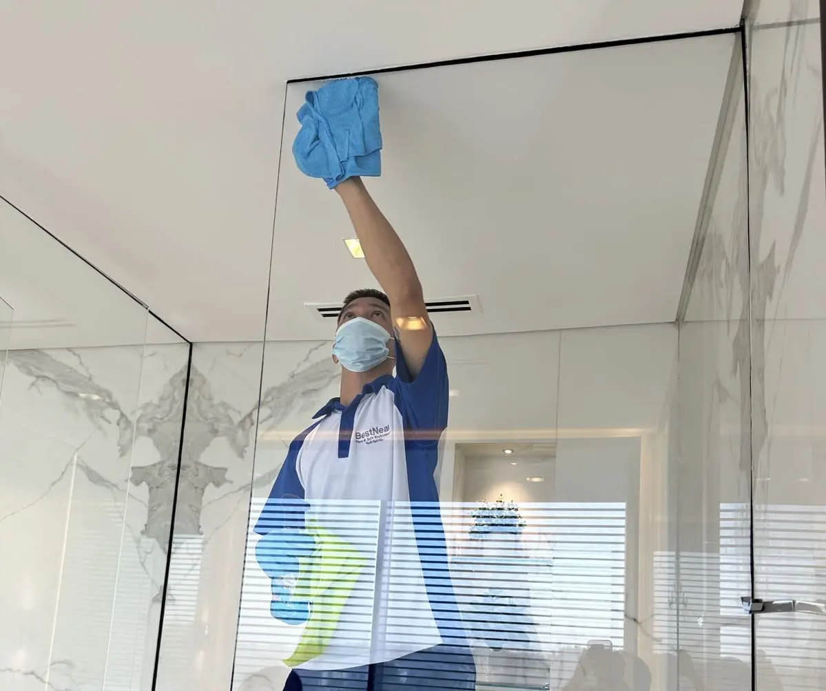 A BestNear technician cleaning a tall glass panel in a marble-clad Dubai home