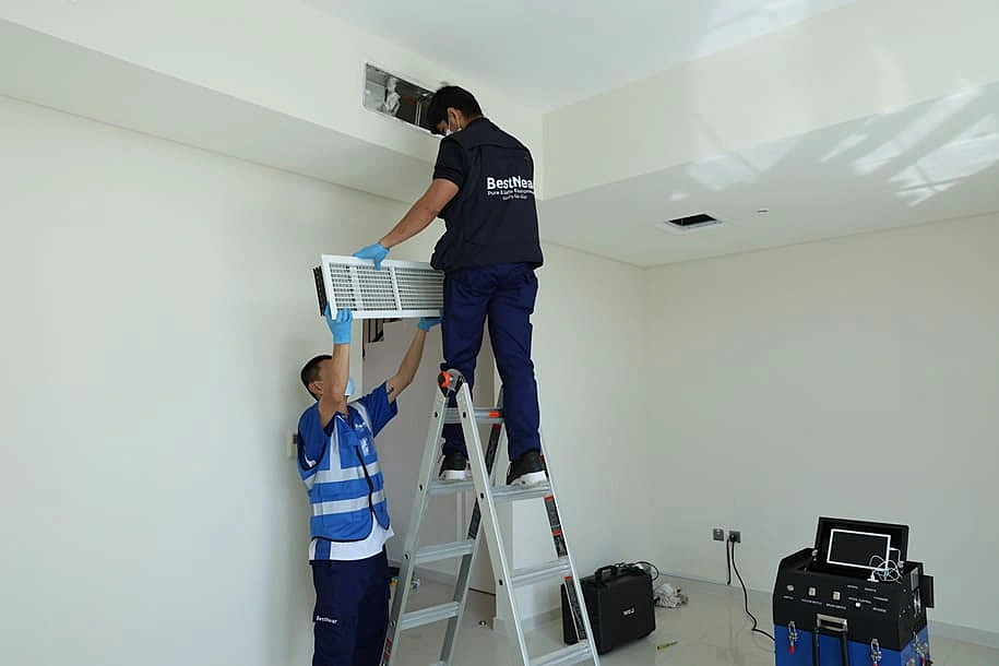 Two BestNear technicians removing a ceiling AC grille in a Dubai apartment